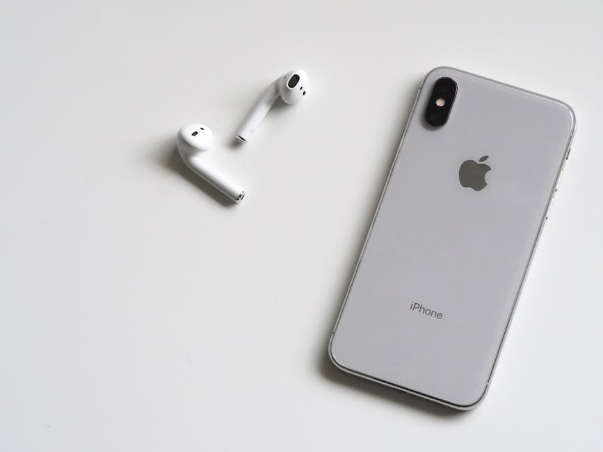 Close-up of a silver iPhone and wireless AirPods on a sleek white background